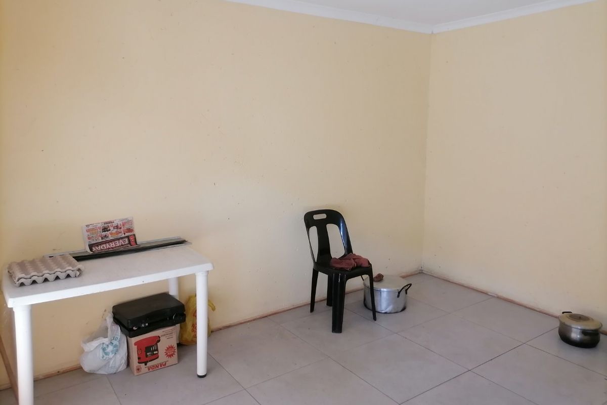 A sparsely furnished living area featuring light-colored tiled flooring and plain walls, presenting a blank canvas for potential interior design updates.