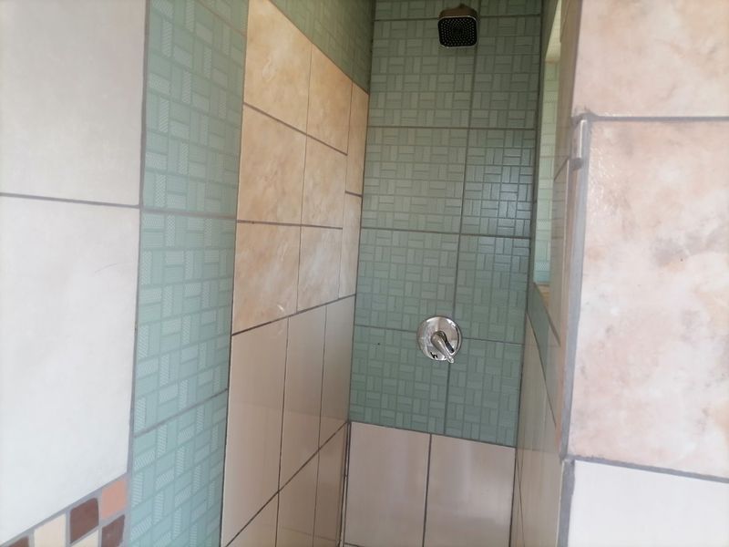 A shower enclosure featuring a modern square shower head, chrome mixer tap, and a combination of green and beige decorative wall tiles.