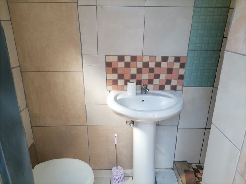 A small bathroom featuring a pedestal basin and multi-colored ceramic wall tiling.