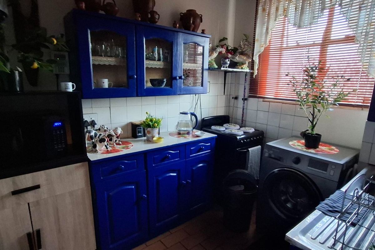 A functional kitchen featuring blue cabinetry, tiled backsplash, and a stainless steel sink, offering a practical layout with natural light from the window.
