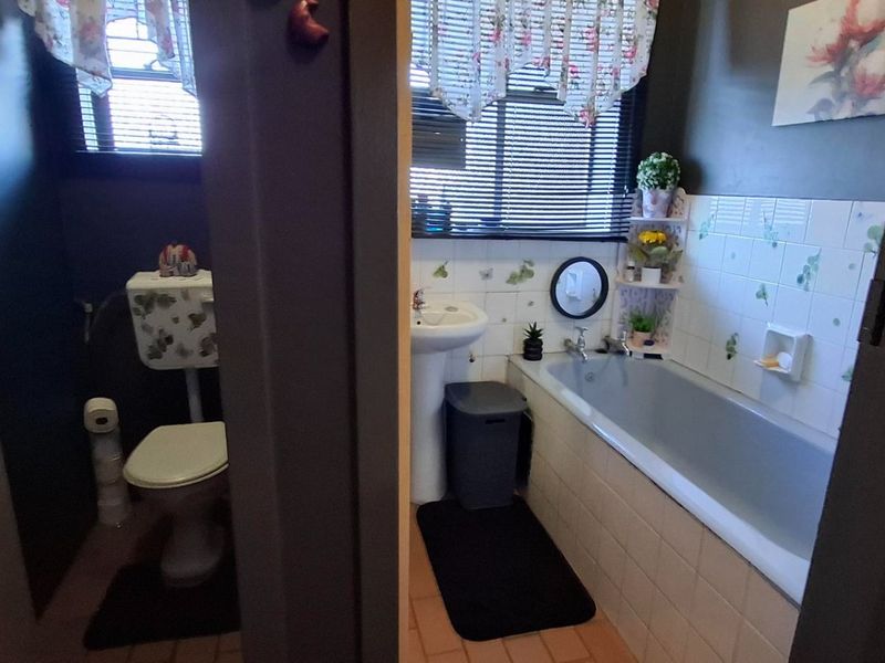 A functional bathroom featuring a pedestal basin, bathtub with tiled splashback, and a separate toilet area with window blinds.