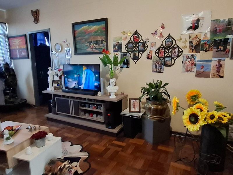 A living room featuring classic parquet flooring and large windows with venetian blinds, offering a functional space with potential for modernization.