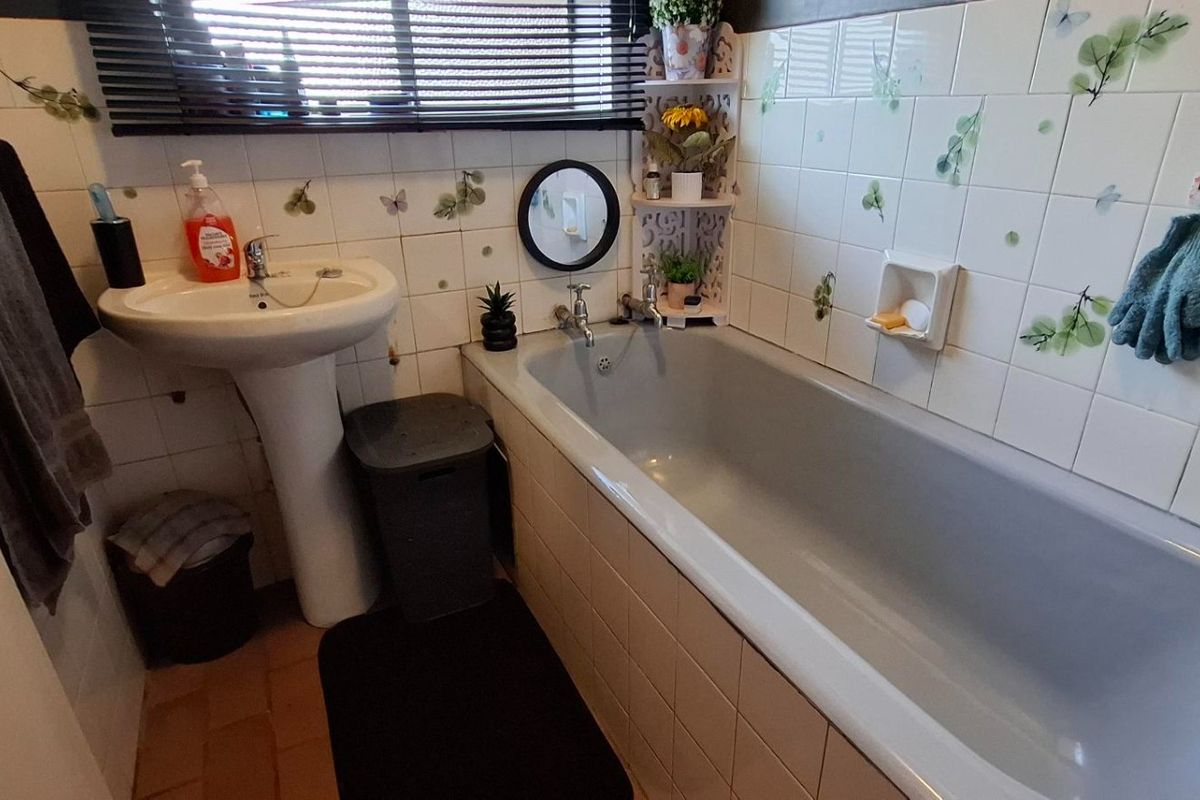 A compact bathroom featuring a pedestal basin, a standard bathtub, and decorative tiled walls with a window blind.