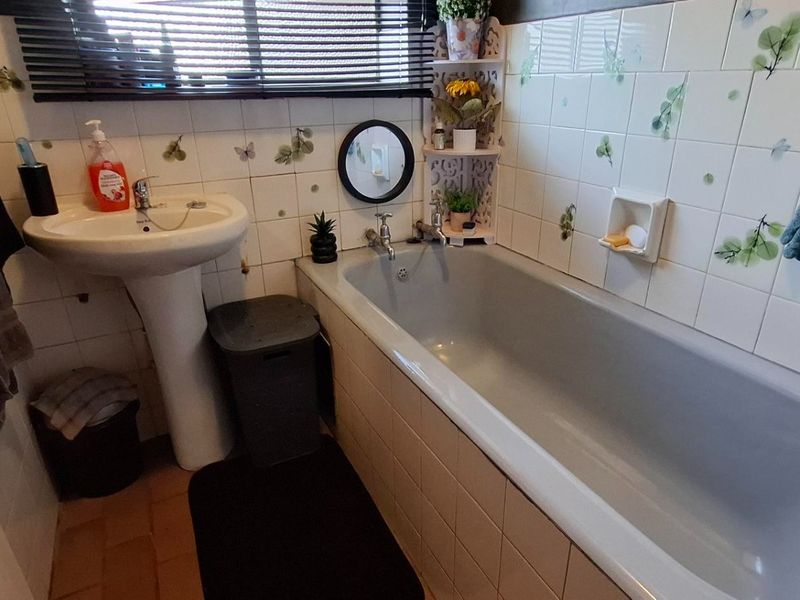 A compact bathroom featuring a pedestal basin, a standard bathtub, and decorative tiled walls with a window blind.