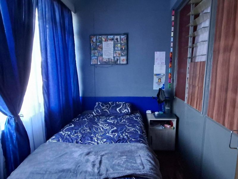 A compact bedroom featuring louvered windows and a built-in partition wall, providing a functional sleeping space.