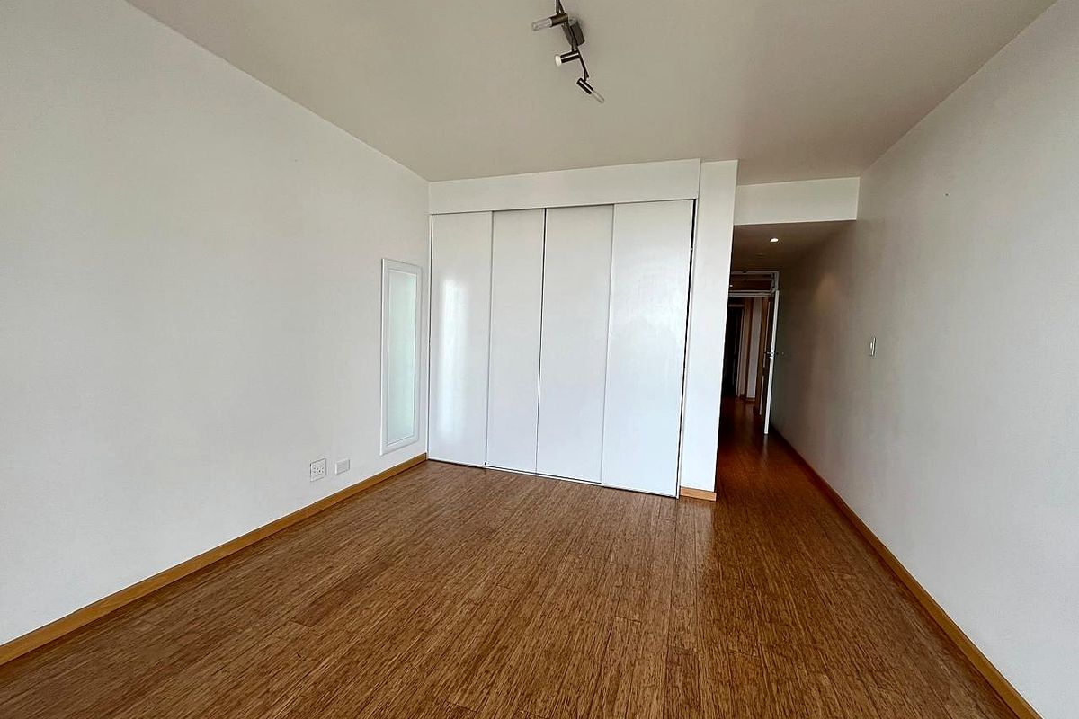 A bright, empty bedroom featuring modern laminate flooring, built-in cupboards, and clean white walls, offering a versatile space ready for personalization.