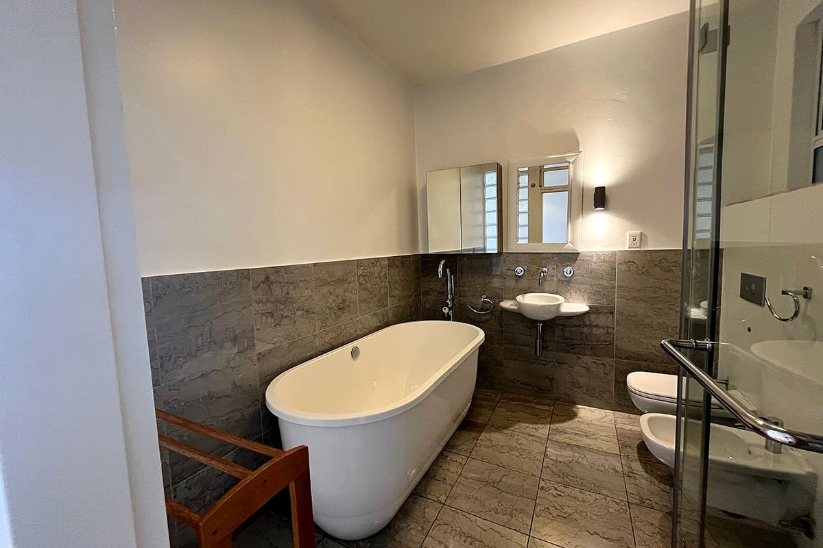 Modern bathroom featuring a freestanding bathtub, wall-mounted basin, bidet, toilet, and a glass-enclosed shower with neutral stone-look tiling.