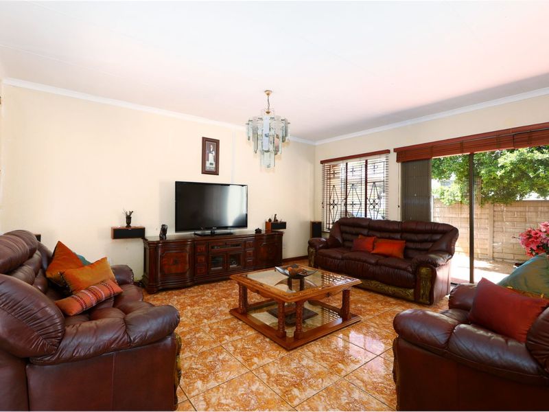 A spacious living room featuring ceramic tile flooring, a crystal chandelier, and large sliding glass doors providing access to the outdoor area.