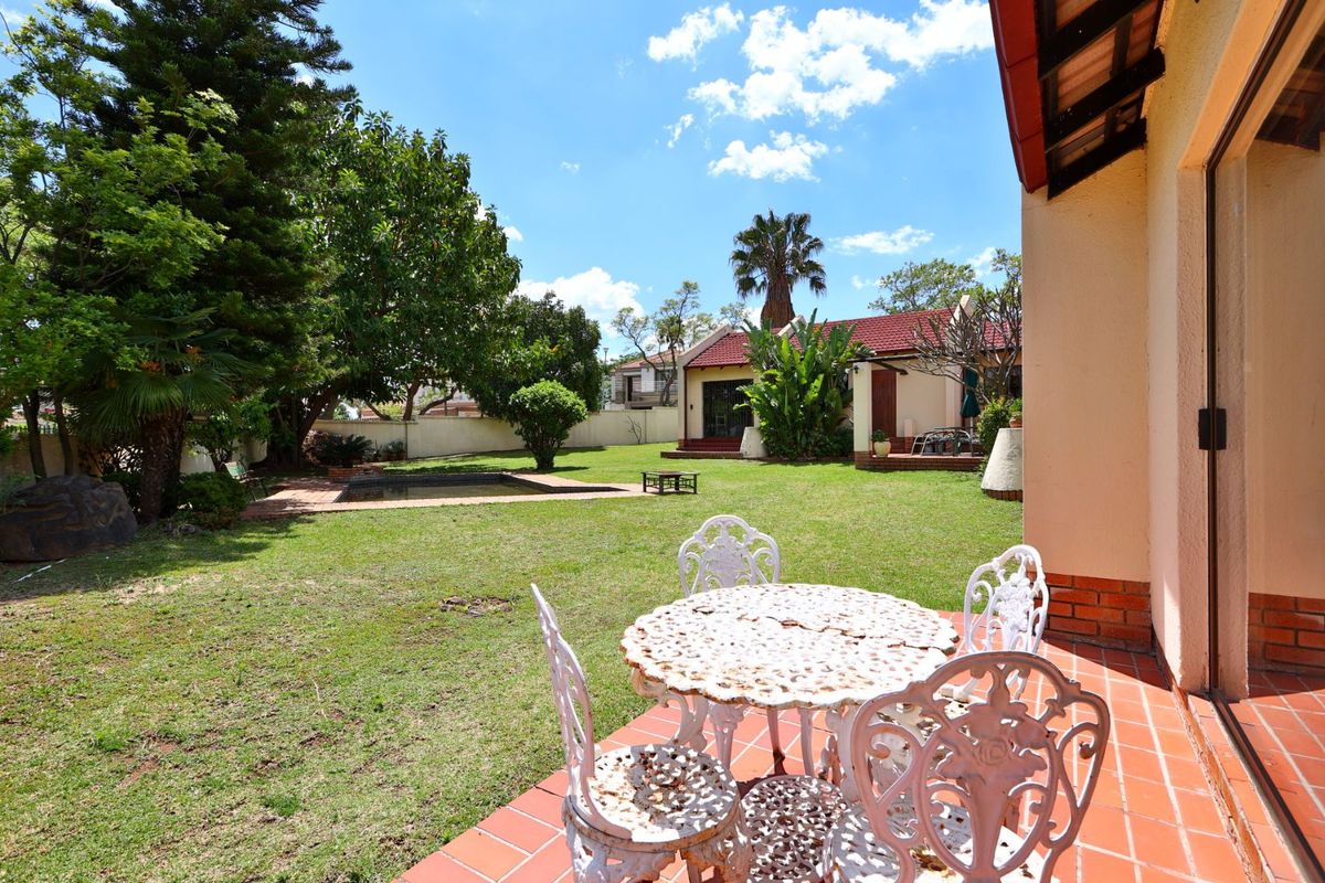A spacious rear garden featuring a tiled patio area, a swimming pool, and established landscaping, providing a private outdoor space for relaxation.