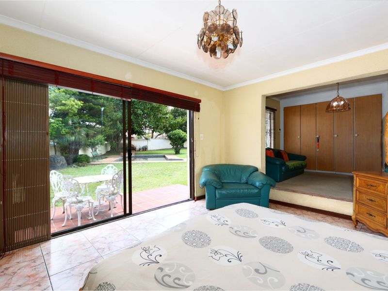 Spacious bedroom featuring a raised platform area, built-in cupboards, and large sliding glass doors providing direct access to the garden and pool area.