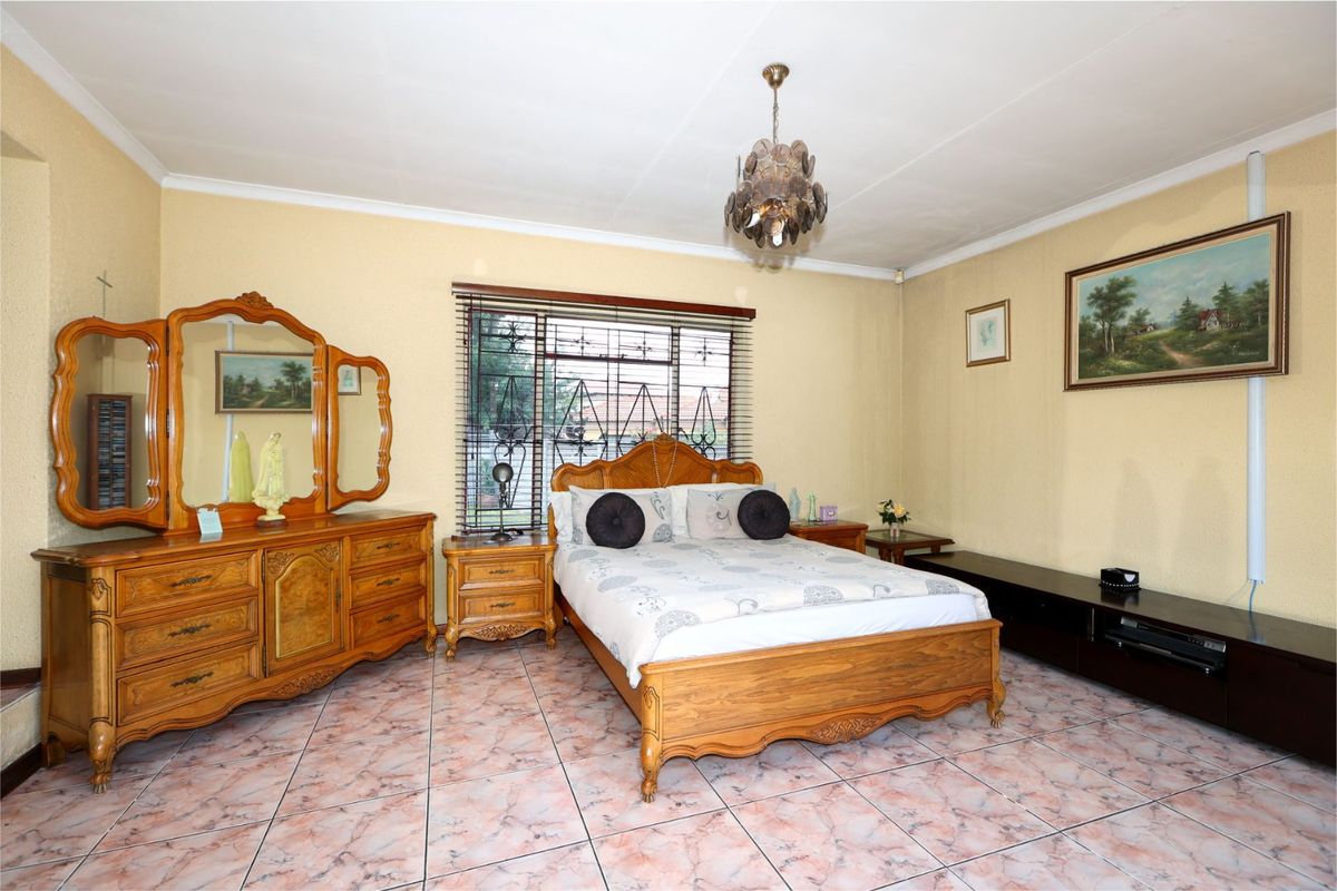 A spacious bedroom featuring tiled flooring, security bars on the window, and a central ceiling light fixture.