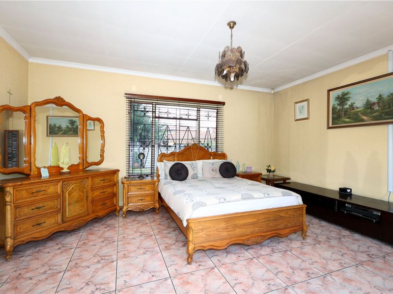 A spacious bedroom featuring tiled flooring, security bars on the window, and a central ceiling light fixture.