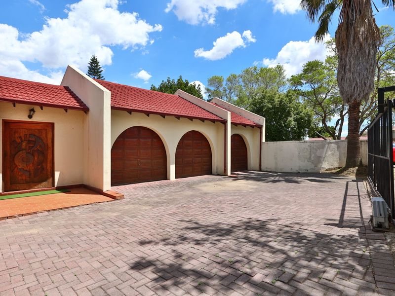 Front exterior view featuring a triple garage with arched doors, a paved driveway, and a distinctive carved wooden entrance door.