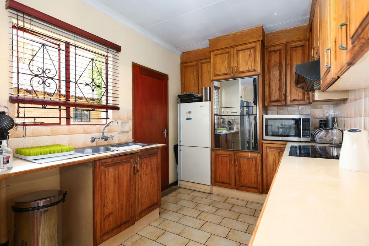 Functional kitchen featuring traditional wooden cabinetry, laminate countertops, built-in oven, electric hob, and tiled flooring with a window overlooking the exterior.