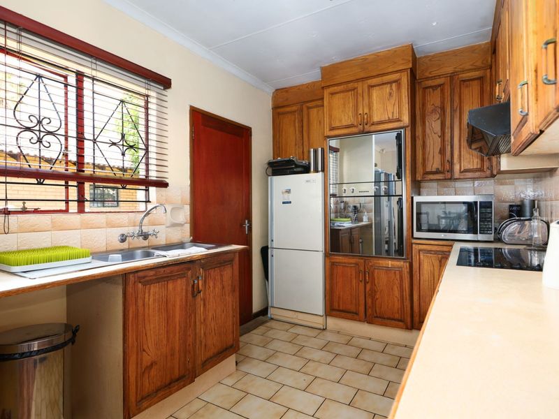 Functional kitchen featuring traditional wooden cabinetry, laminate countertops, built-in oven, electric hob, and tiled flooring with a window overlooking the exterior.