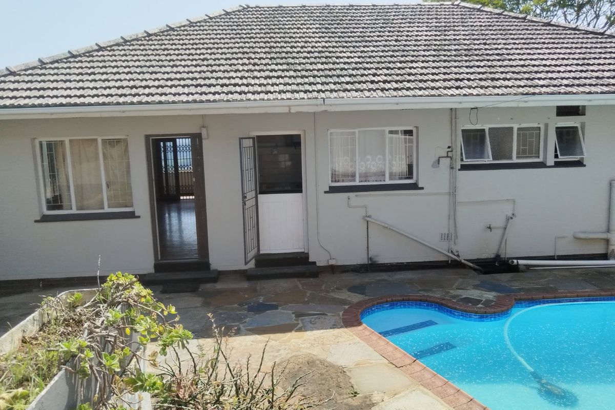 Rear view of the property featuring a tiled roof, stone patio area, and a swimming pool with direct access to the interior.