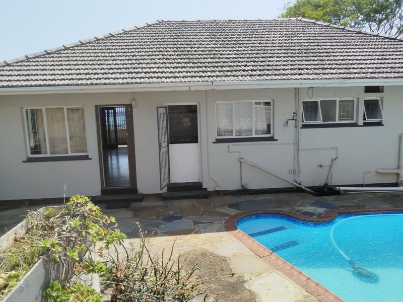 Rear view of the property featuring a tiled roof, stone patio area, and a swimming pool with direct access to the interior.