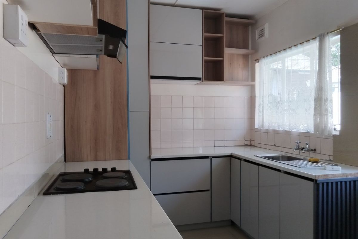 A functional kitchen featuring modern grey cabinetry, wood-look accents, a built-in electric hob with extractor, and a stainless steel sink with tiled backsplash.
