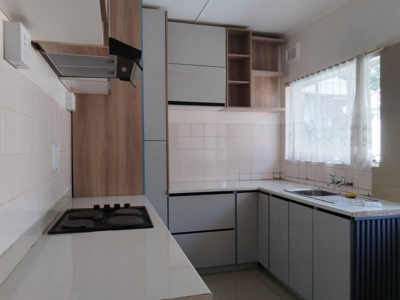 A functional kitchen featuring modern grey cabinetry, wood-look accents, a built-in electric hob with extractor, and a stainless steel sink with tiled backsplash.