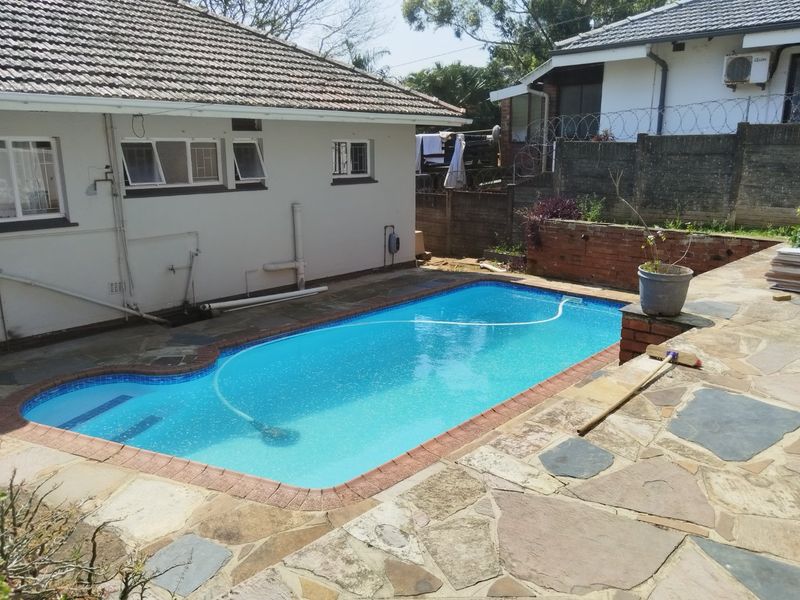 Outdoor pool area featuring a swimming pool with tiled coping, surrounded by a crazy paving stone patio and a brick retaining wall.