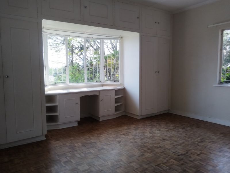 Spacious bedroom featuring classic parquet flooring, extensive built-in cabinetry, and a charming bay window with an integrated vanity area.