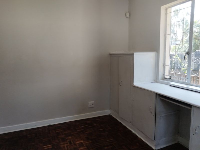 A vacant bedroom featuring original parquet flooring, built-in storage cabinetry, and a window fitted with security bars.