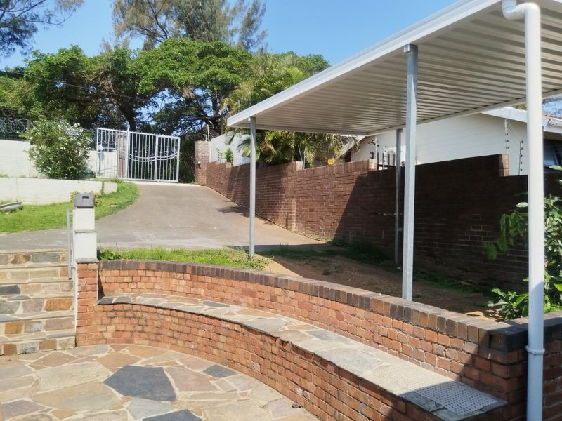 Front exterior area featuring a paved driveway, metal carport, brick retaining wall with built-in seating, and secure gated access.