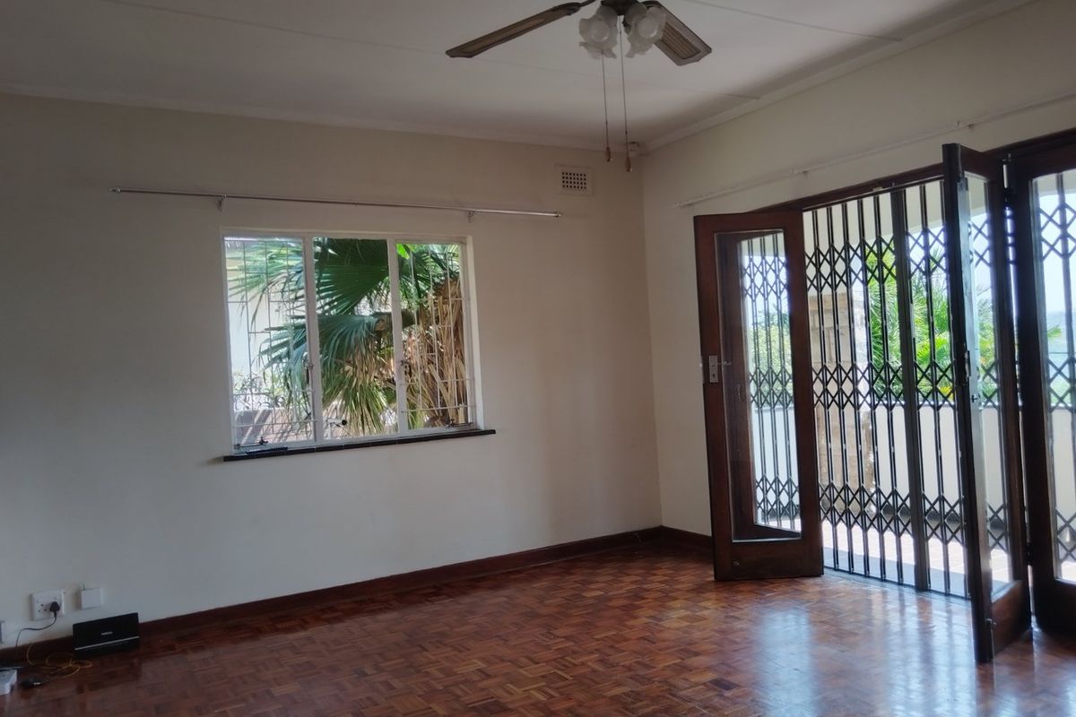 A bright, empty living room featuring classic parquet flooring, a ceiling fan, and direct access to an outdoor area through a secure timber door.