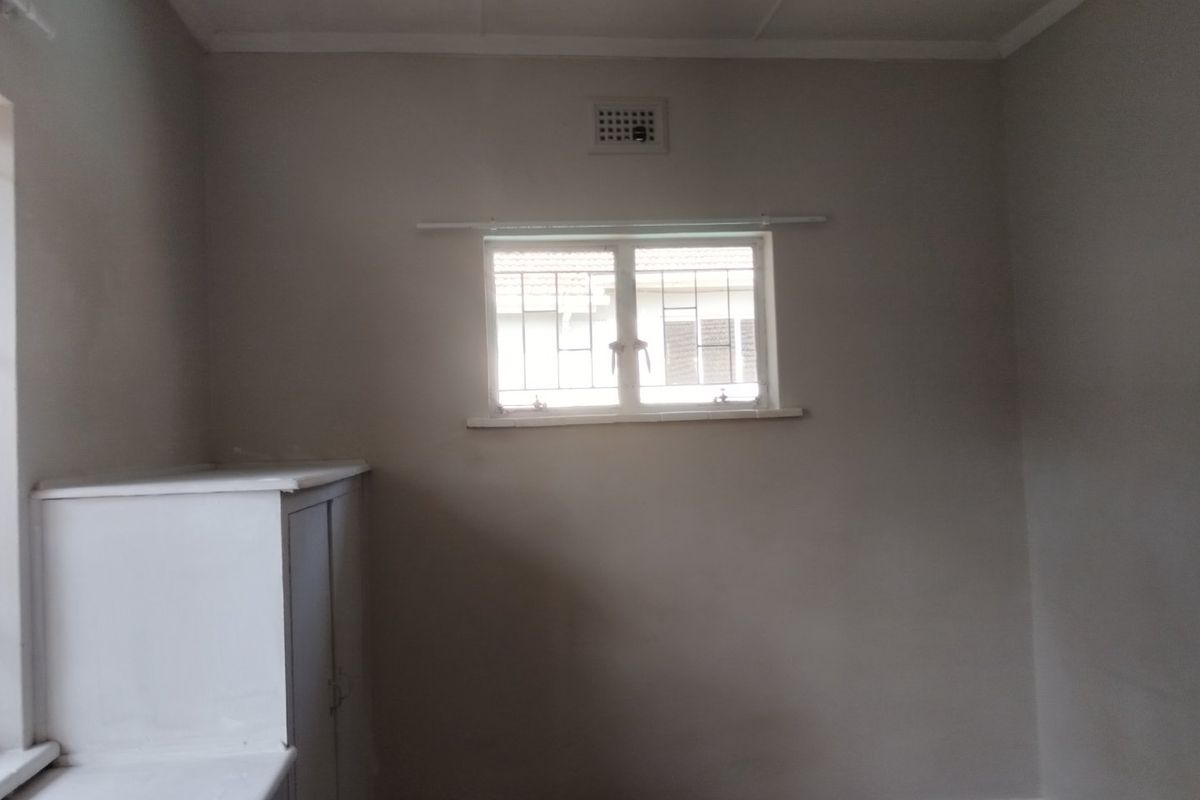 An empty bedroom featuring neutral walls, a built-in cupboard, and a window fitted with security bars.