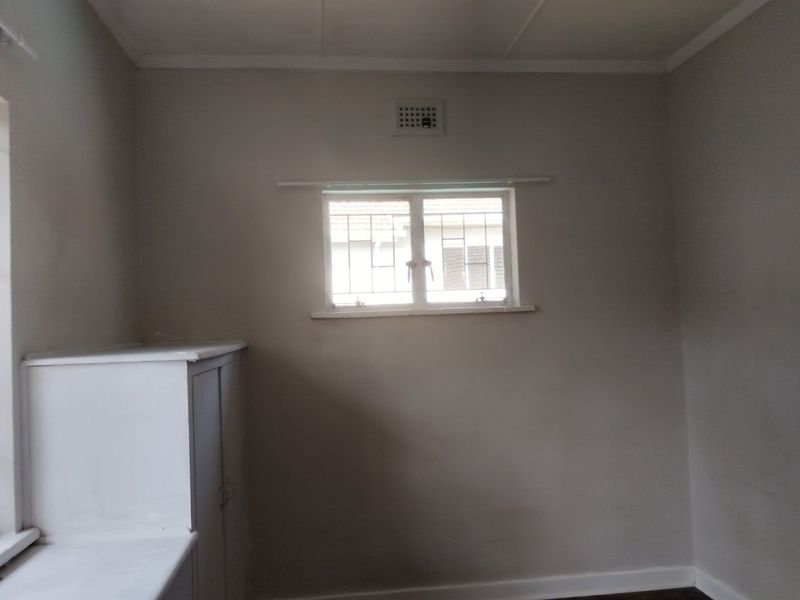 An empty bedroom featuring neutral walls, a built-in cupboard, and a window fitted with security bars.