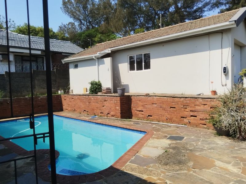 Outdoor pool area featuring a swimming pool, stone paving, and a brick retaining wall against the rear elevation of the house.