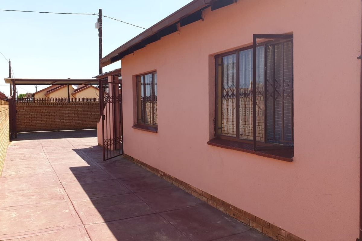 Rear exterior view of the property featuring a paved driveway, security gates, and a carport structure.
