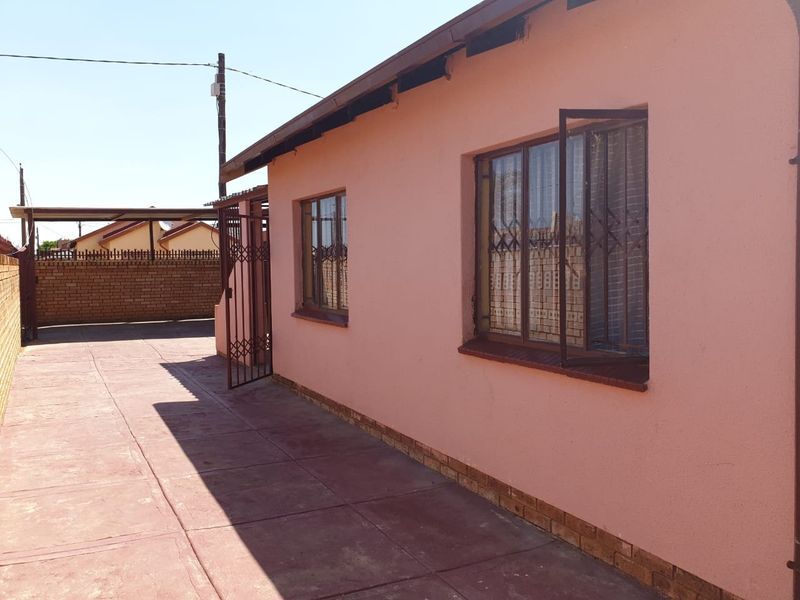Rear exterior view of the property featuring a paved driveway, security gates, and a carport structure.