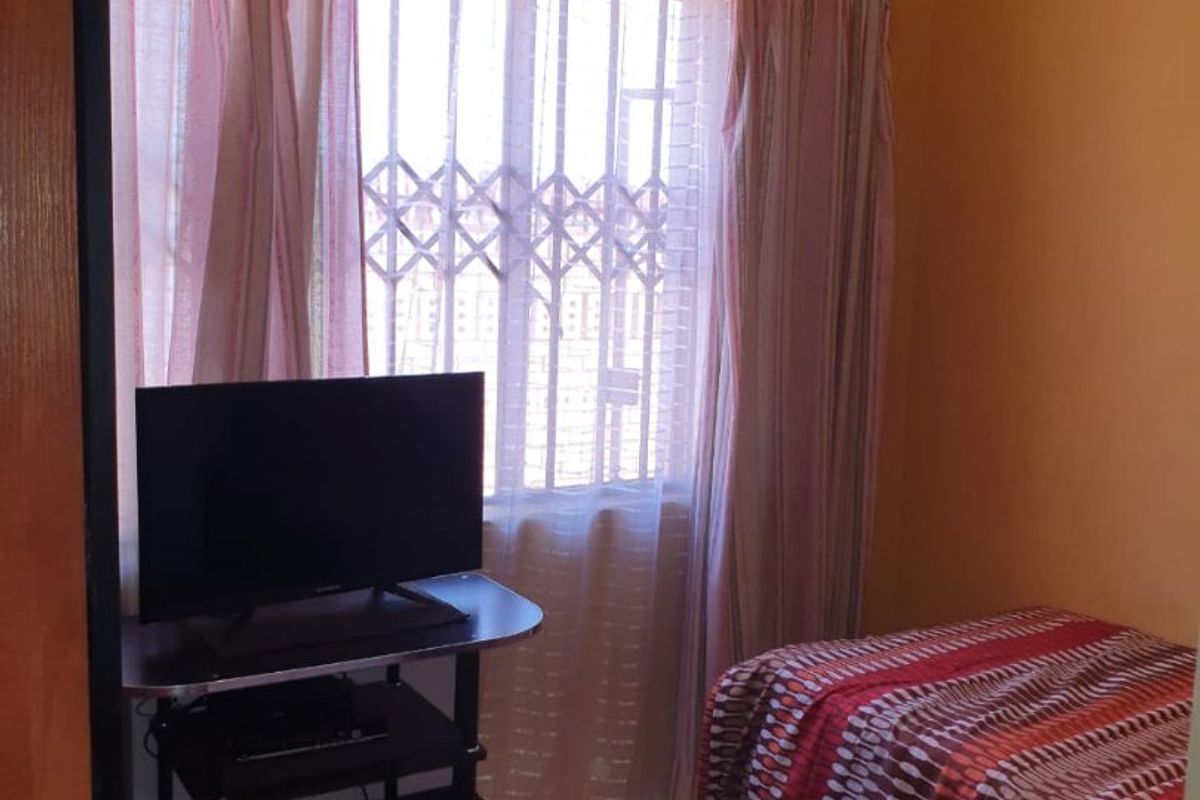 A compact bedroom featuring tiled flooring, a window with a security gate, and decorative ceiling cornicing.