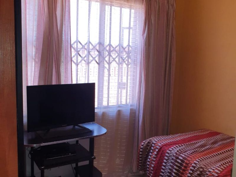 A compact bedroom featuring tiled flooring, a window with a security gate, and decorative ceiling cornicing.