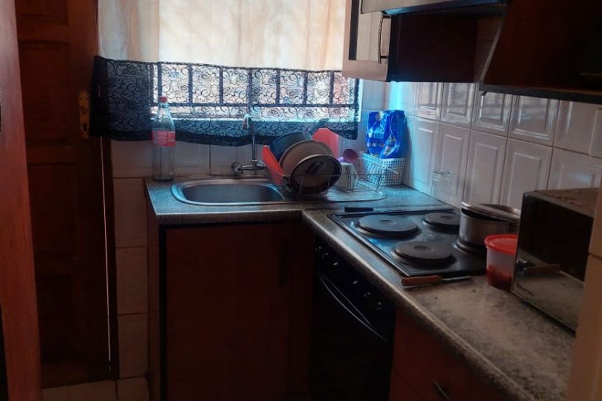 Compact kitchen featuring wooden cabinetry, built-in electric hob, oven, extractor fan, and tiled finishes.