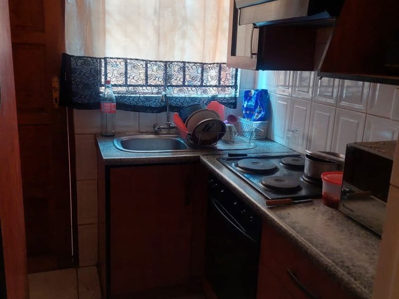 Compact kitchen featuring wooden cabinetry, built-in electric hob, oven, extractor fan, and tiled finishes.
