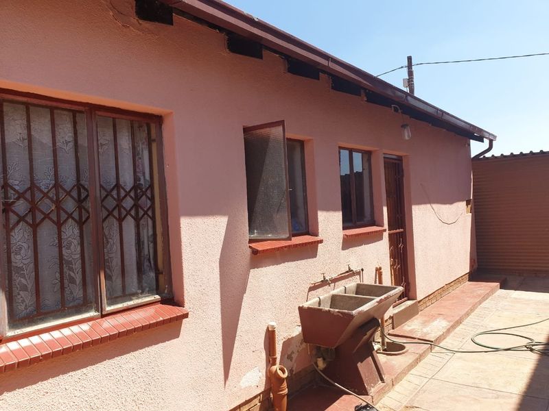Rear exterior view of the property featuring a paved patio area, external laundry sink, and security bars on the windows.