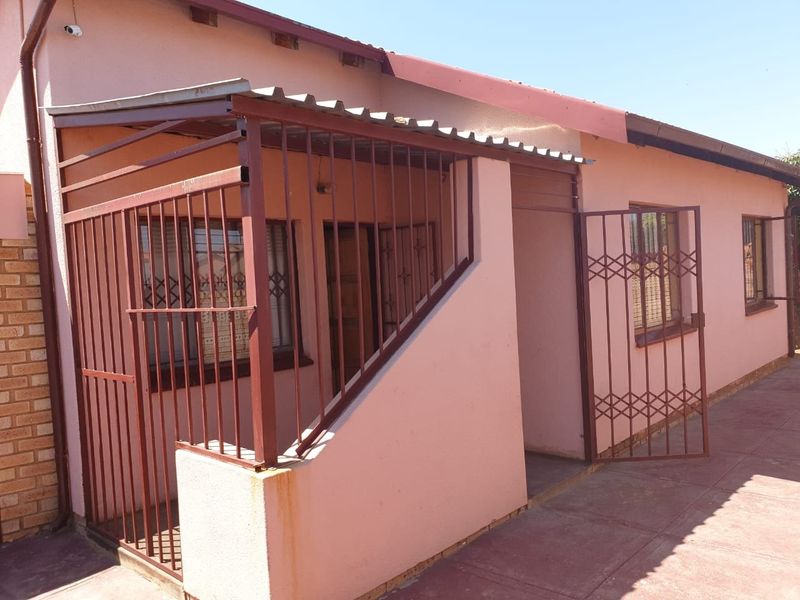 Front exterior view of a single-story house featuring a covered entrance area with security gates and bars, and a paved walkway.
