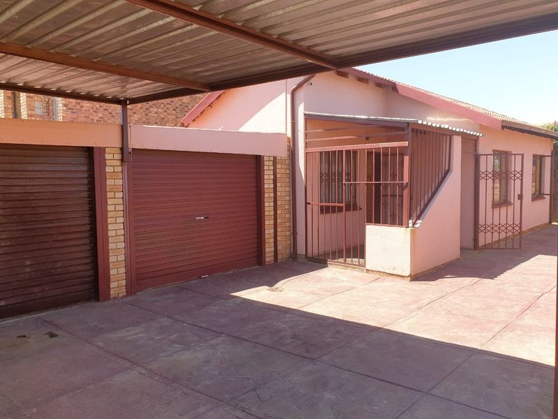 Front exterior view of the house featuring a covered carport, a roller shutter garage door, and secure gated entrance with paved driveway.