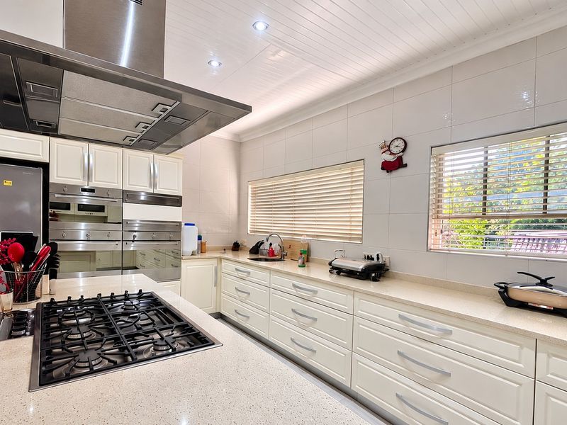 Modern kitchen featuring stone countertops, a gas hob with overhead extractor, built-in ovens, and ample cabinetry, finished with recessed lighting and clean tiled walls.