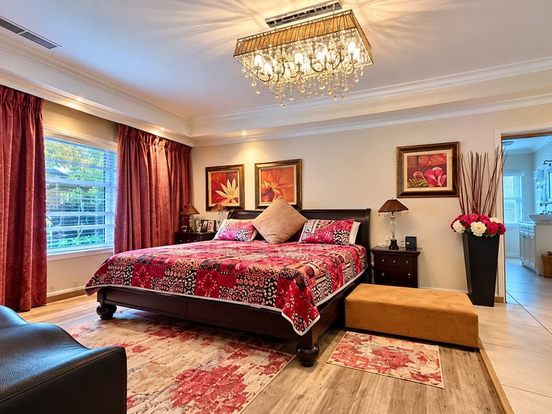 Spacious primary bedroom featuring elegant crown molding, a crystal chandelier, and direct access to an en-suite bathroom with modern laminate flooring throughout.