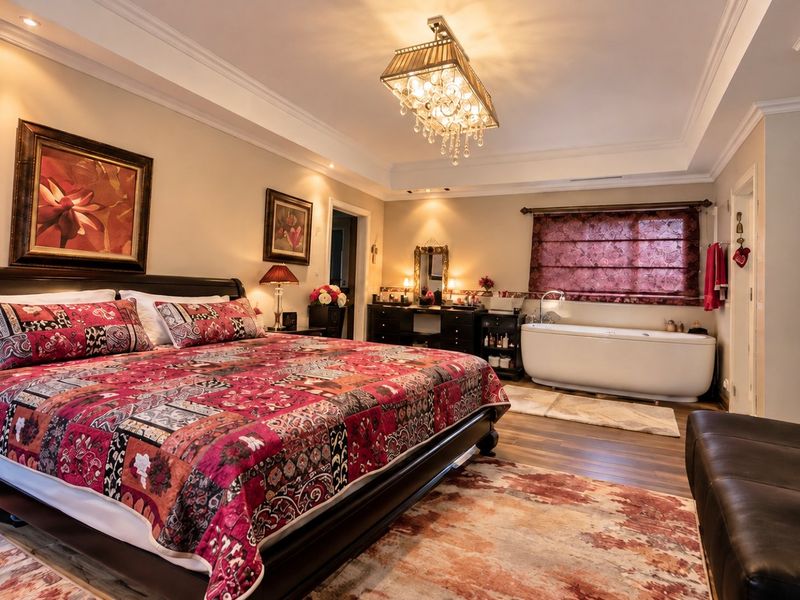 A spacious master bedroom featuring hardwood flooring, crown molding, recessed lighting, a crystal chandelier, and an integrated freestanding bathtub.