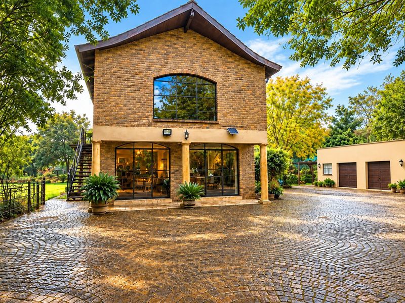 A charming brick farmhouse exterior featuring a cobblestone driveway, arched windows, stone columns, and an external staircase leading to the upper level.