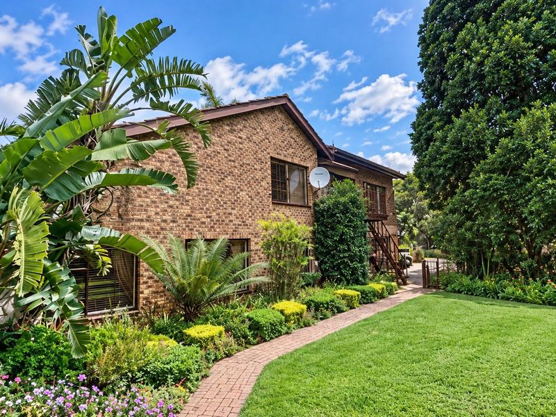 A well-maintained brick farmhouse exterior featuring a lush landscaped garden, paved walkway, and an external metal staircase leading to the upper level.