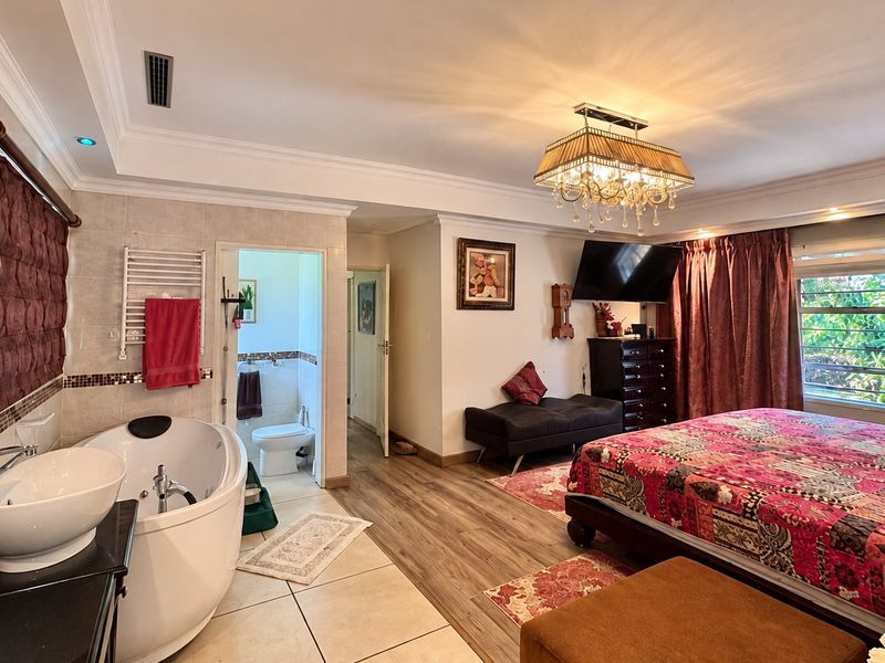 Spacious bedroom featuring an integrated en-suite bathroom area with a freestanding bathtub, vanity basin, and modern tiled and laminate flooring finishes.