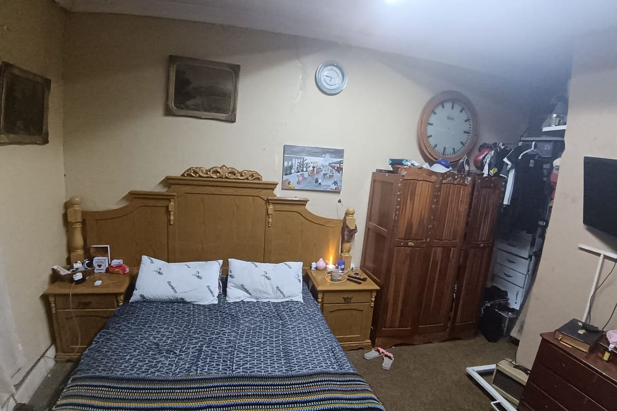 A bedroom featuring a large wooden headboard and built-in storage space, showing signs of wear and requiring cosmetic updates to the wall finishes.