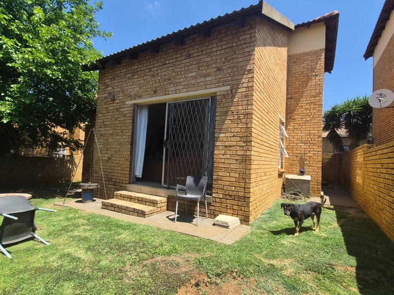 Rear view of the apartment featuring a face brick facade, sliding glass door with security gate, and a private garden area.
