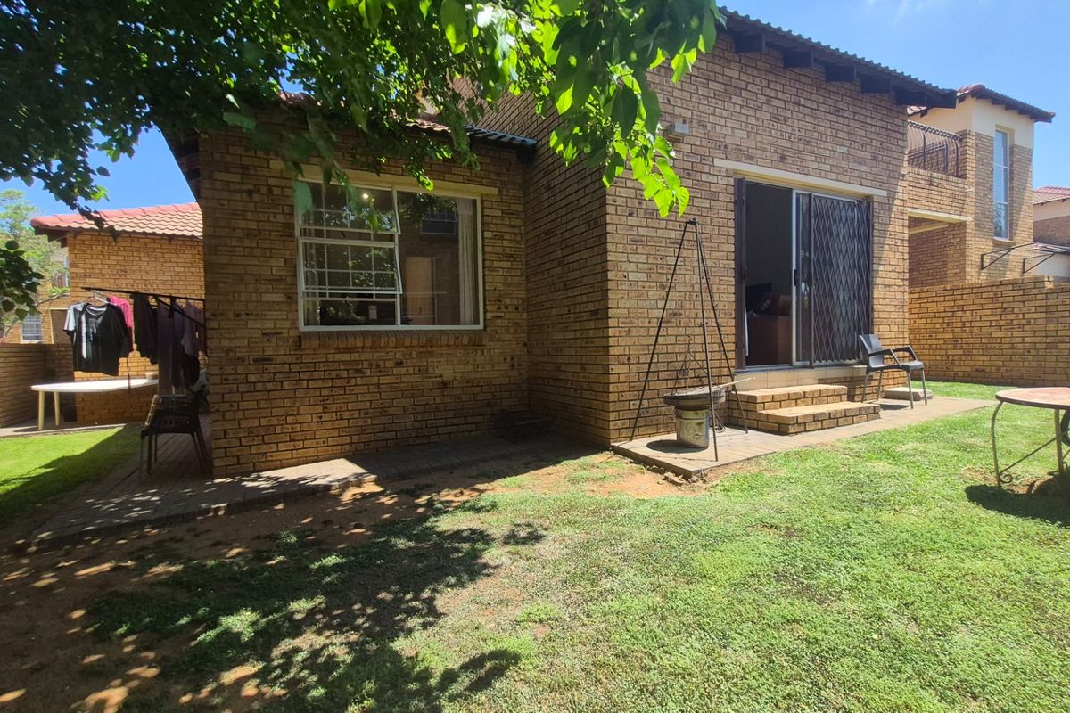 Rear view of a face brick apartment featuring a private garden, paved patio area, and sliding door access to the interior living space.