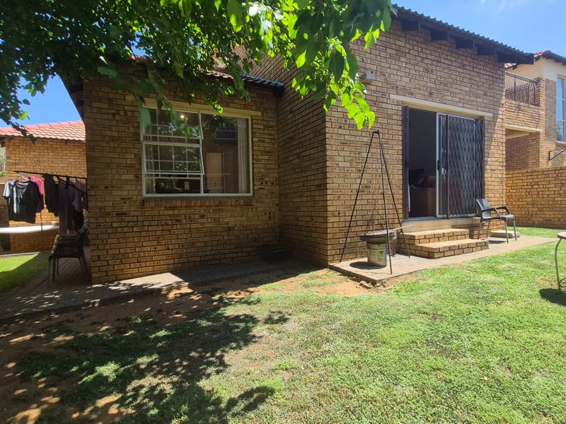 Rear view of a face brick apartment featuring a private garden, paved patio area, and sliding door access to the interior living space.
